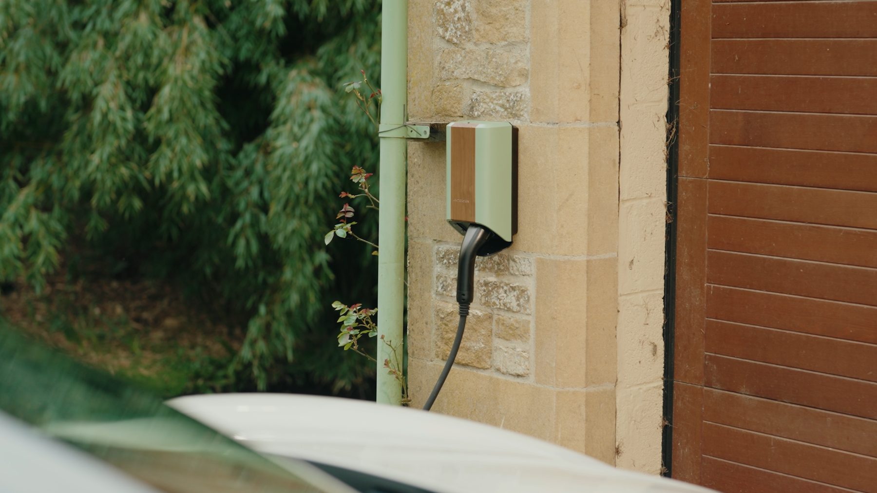 Andersen EV charger in sage green and wood finish, mounted on a stone wall on a driveway